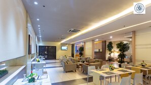 A modern hotel lobby with multiple seating areas, including tables and chairs, and a television mounted on the wall. - La Breza Hotel (Quezon City)