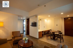 A hotel room with a sofa, armchair, dining table, and a TV mounted on the wall. - La Breza Hotel (Quezon City)