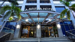 The entrance of the Breza Hotel with a glass canopy, palm trees, and a signboard advertising an acoustic night event. - La Breza Hotel (Quezon City)