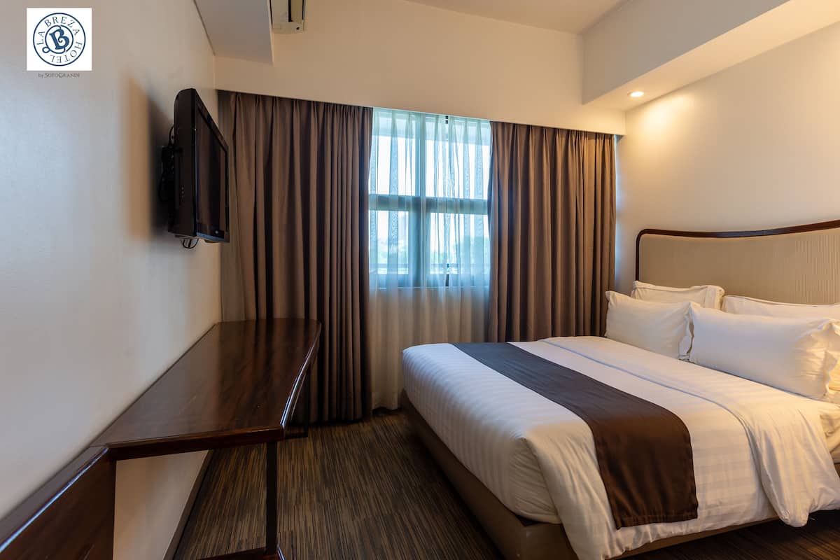 A hotel room with a bed, a desk, a television, and a window with curtains.