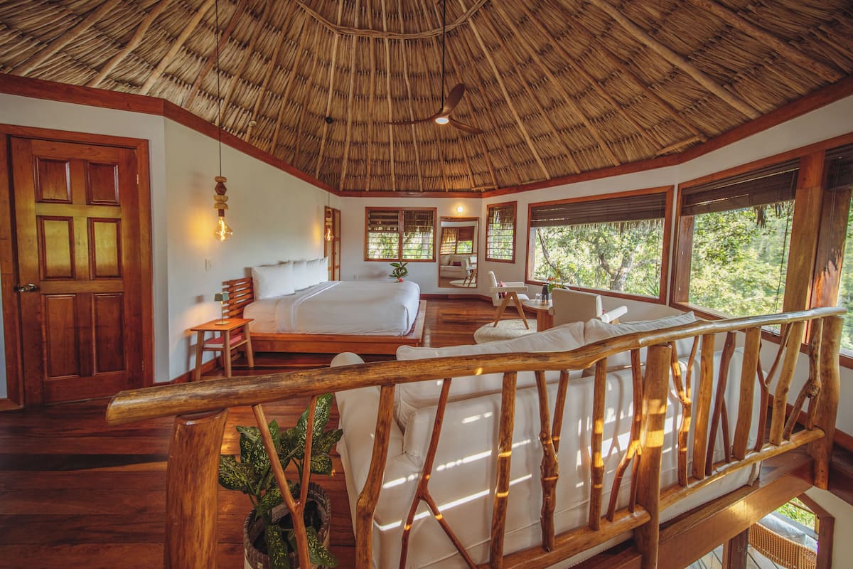 A room with a thatched roof, wooden furniture, a bed, a desk, and large windows.