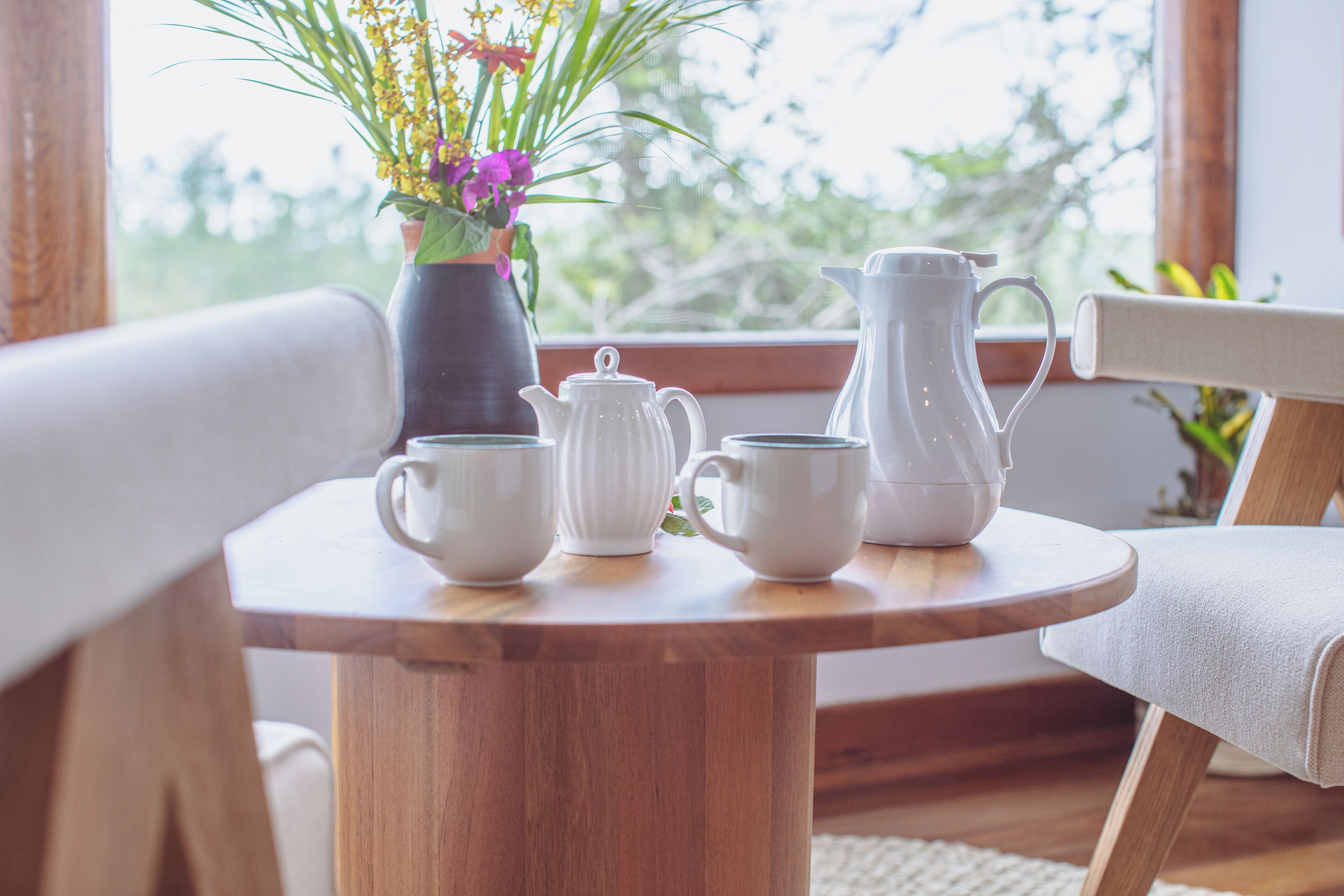 A wooden table with a vase of flowers, a teapot, two cups, and a pitcher.