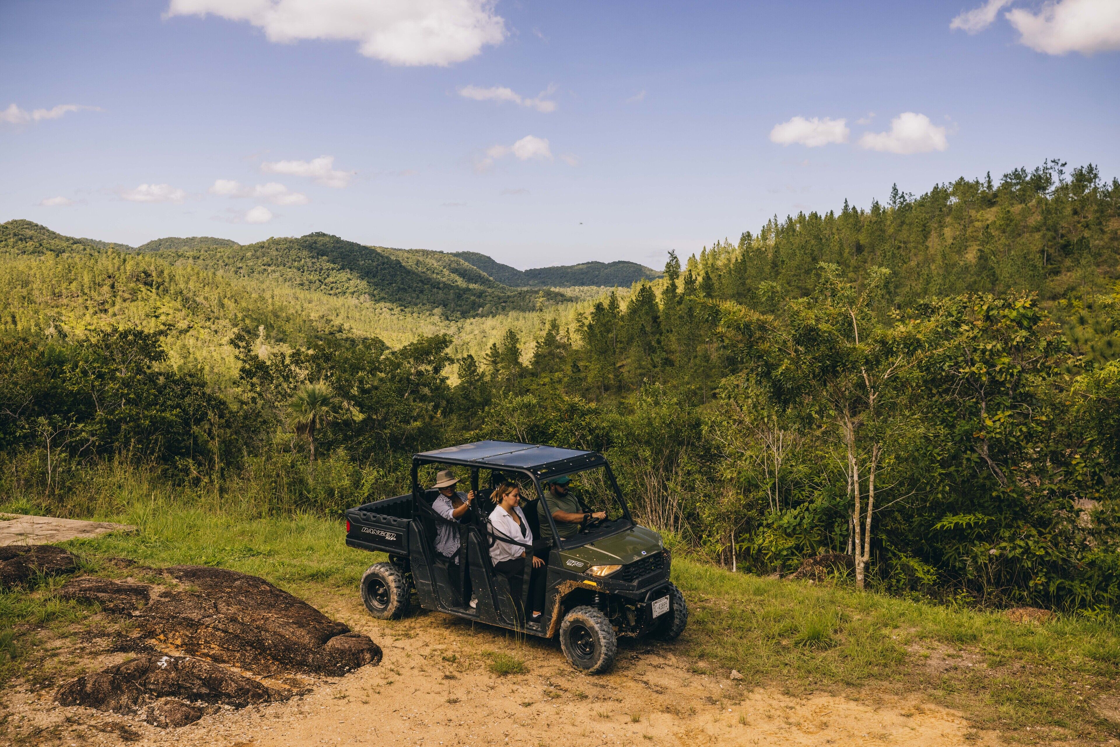 A vehicle on a dirt path surrounded by lush greenery and hills.