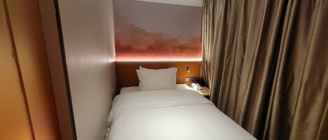 A hotel room with a bed, a nightstand, a phone, and a wall with a sunset mural.