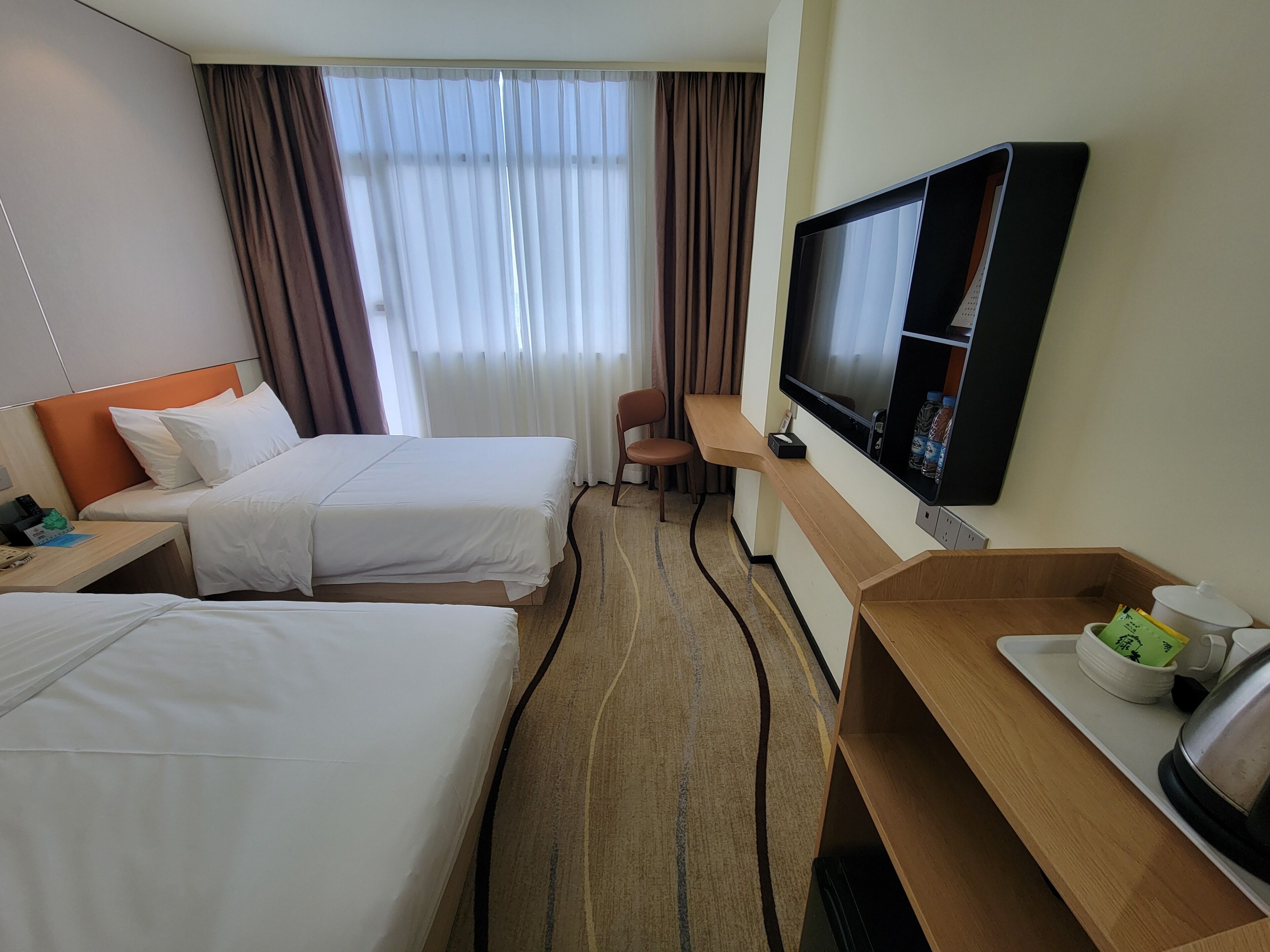 Een hotelkamer met twee bedden, een bureau met een televisie, een stoel en een dienblad met een waterkoker en kopjes.