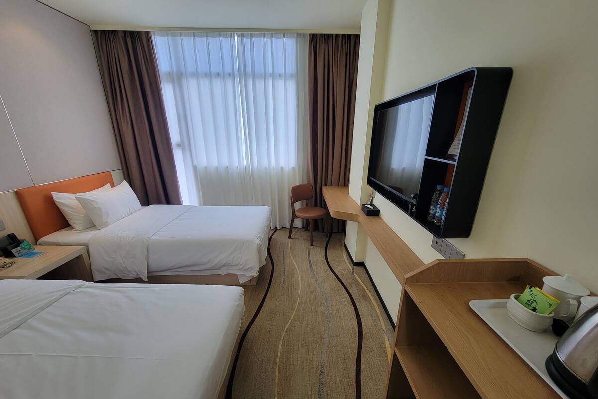 Une chambre d’hôtel avec deux lits, un bureau avec une télévision, une chaise et un plateau avec une bouilloire et des tasses.
