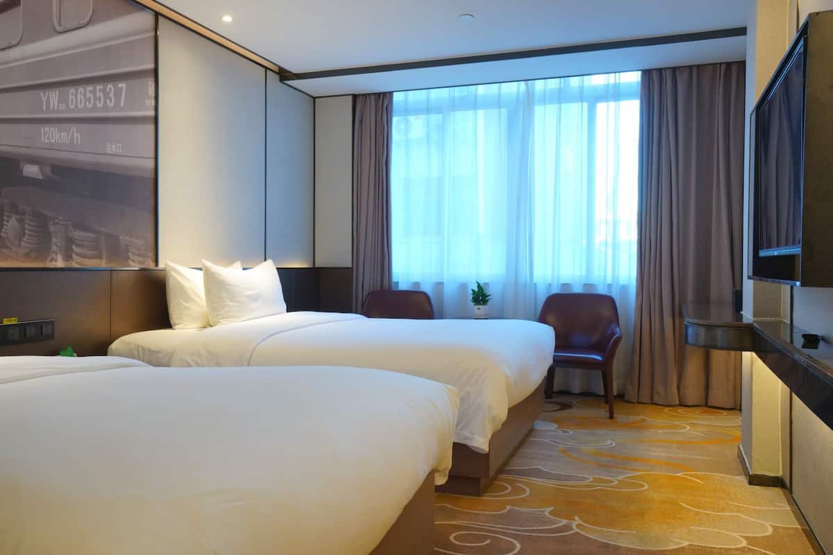 A hotel room with two beds, a TV, a desk, and a window with curtains.