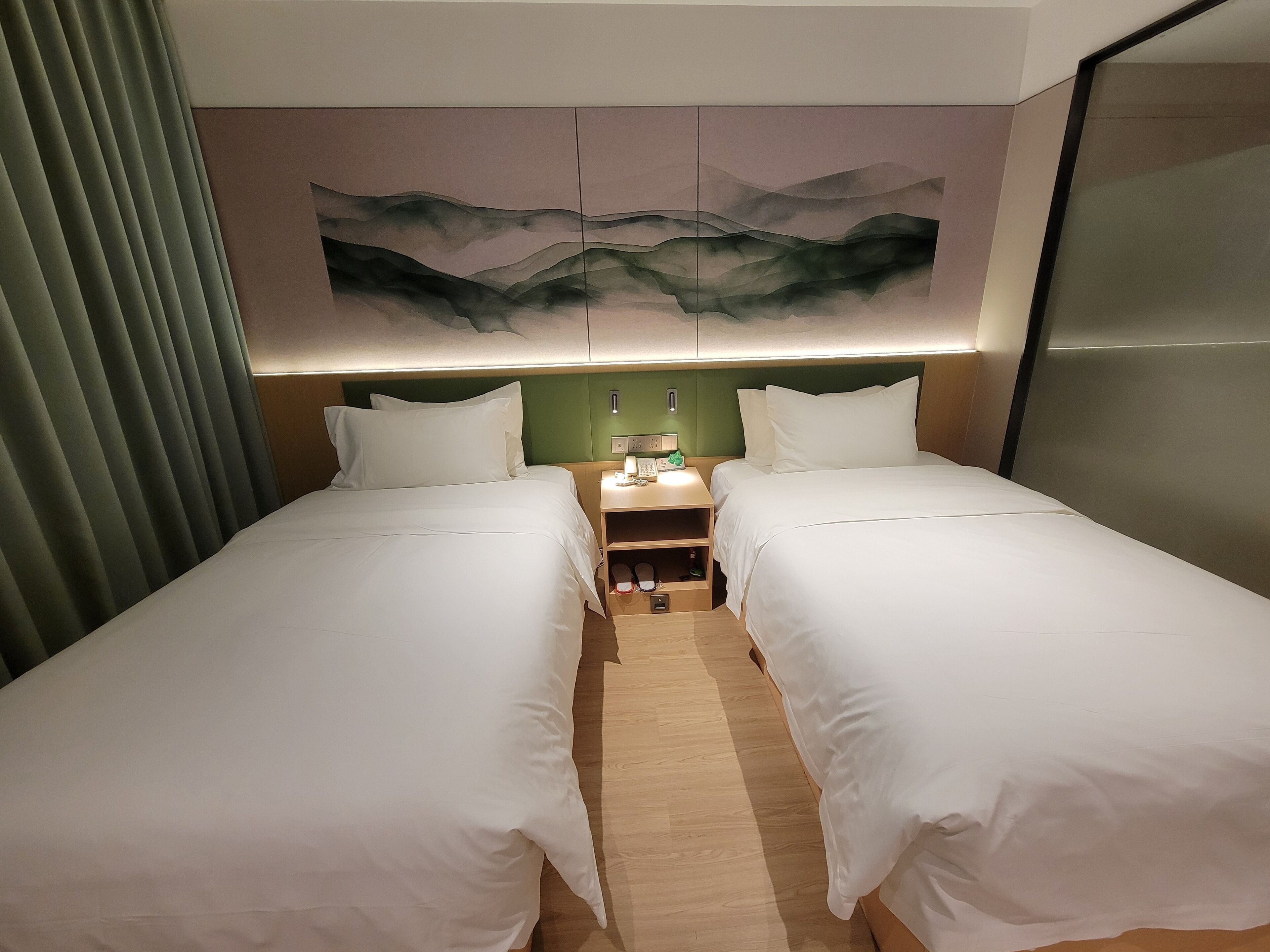 Une chambre d’hôtel avec deux lits simples, une table de chevet avec une lampe et un tableau accroché au mur.