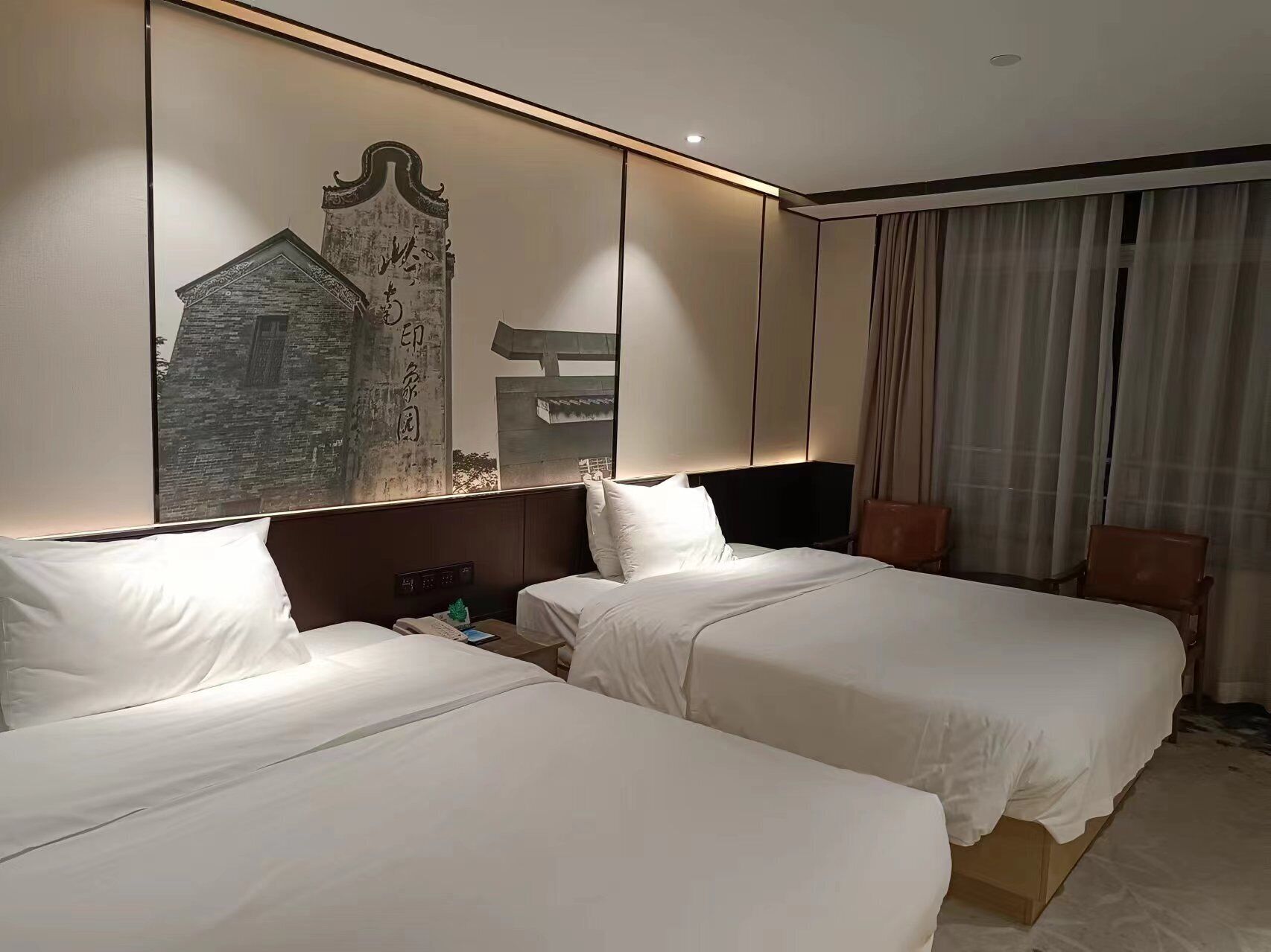 Een hotelkamer met twee bedden, een groot wanddecor, een televisie en een raam met gordijnen.