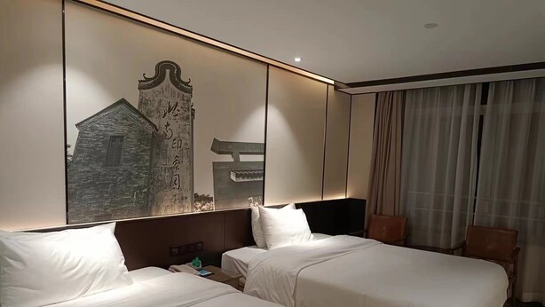 Ein Hotelzimmer mit zwei Betten, einem großen Wandbild, einem Fernseher und einem Fenster mit Vorhängen.