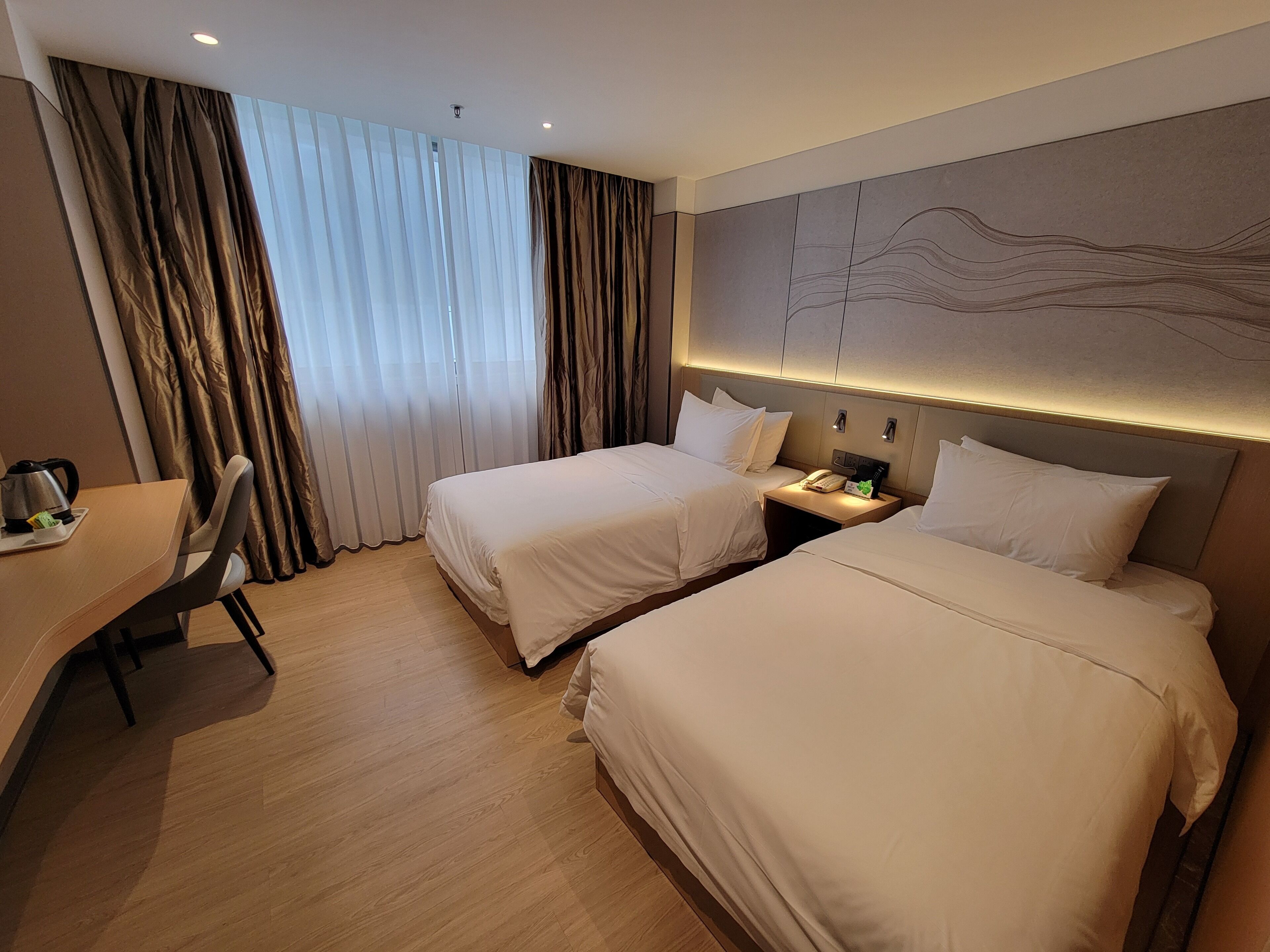 Habitación de hotel con dos camas, un escritorio y un ventanal grande con cortinas.