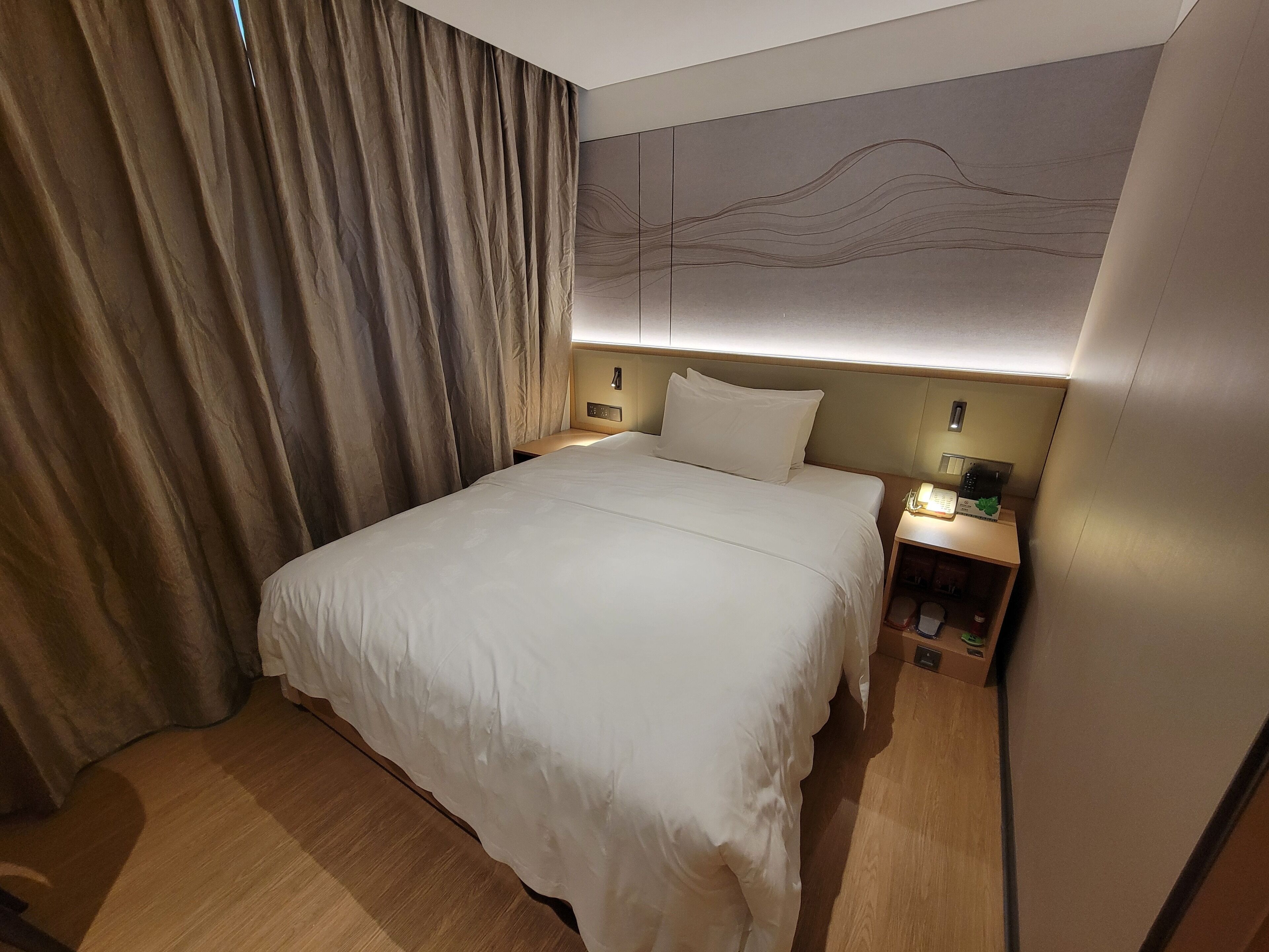 Une chambre d’hôtel avec un grand lit, une table de chevet avec une lampe et un téléphone fixé au mur.