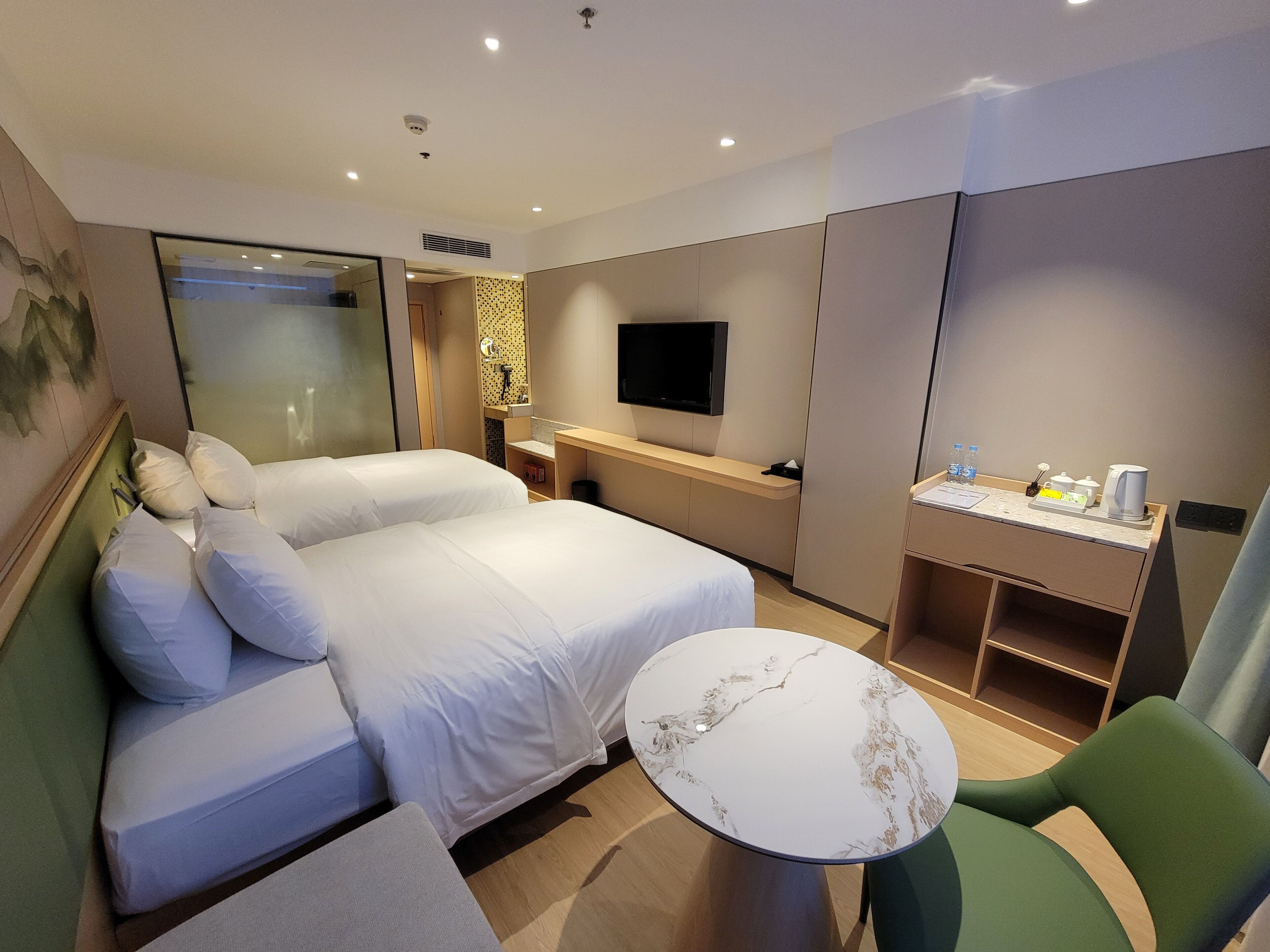 A hotel room with a bed, a desk, a chair, a TV, and a small table.