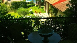 A balcony with a view of the sea, surrounded by greenery and a small table.