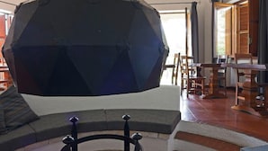 A stone fireplace with a black chimney, a round stone table in front, and a dining area with wooden furniture.
