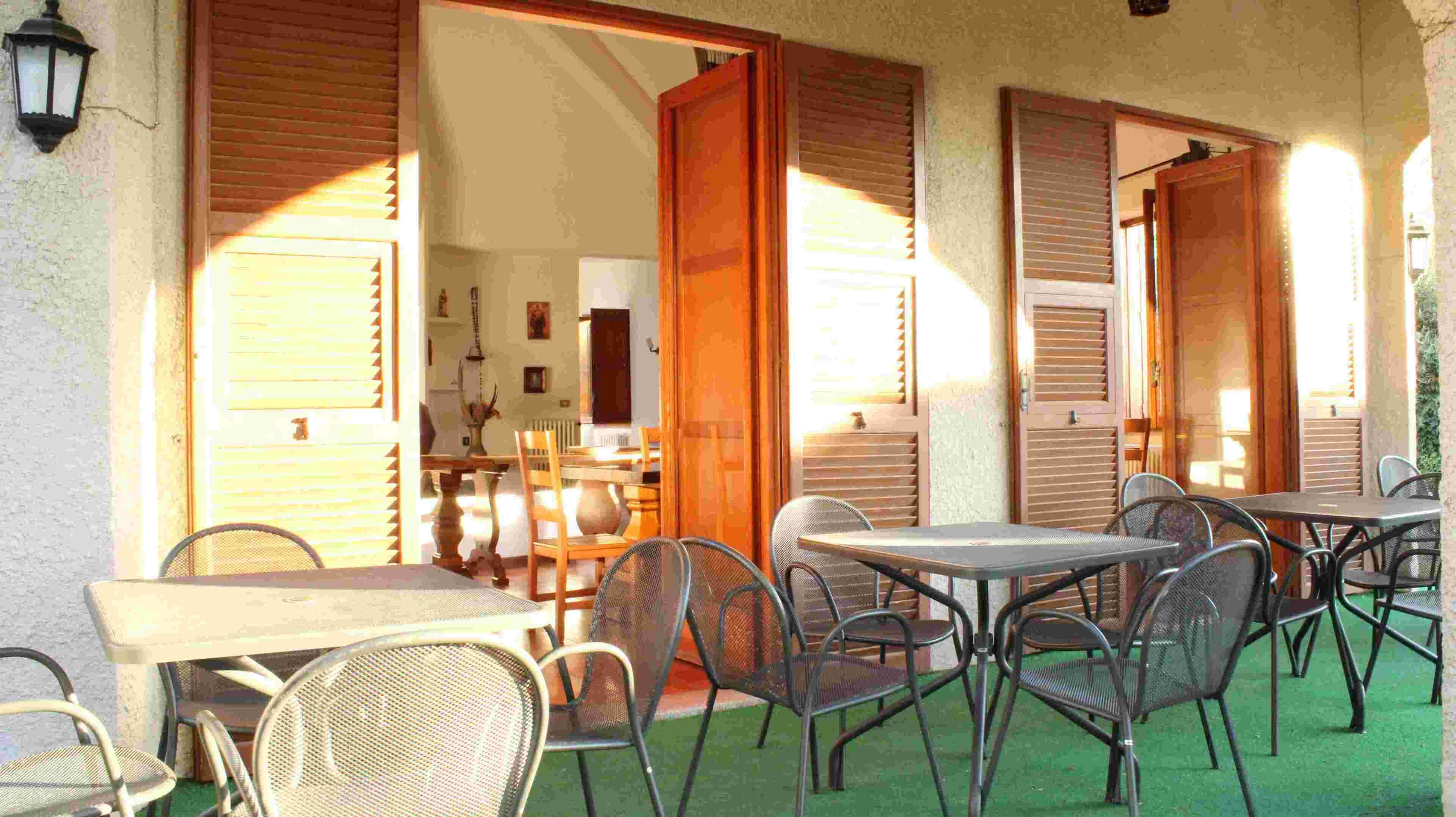 Un área de comedor al aire libre con mesas y sillas, contraventanas de madera y vista hacia el interior.