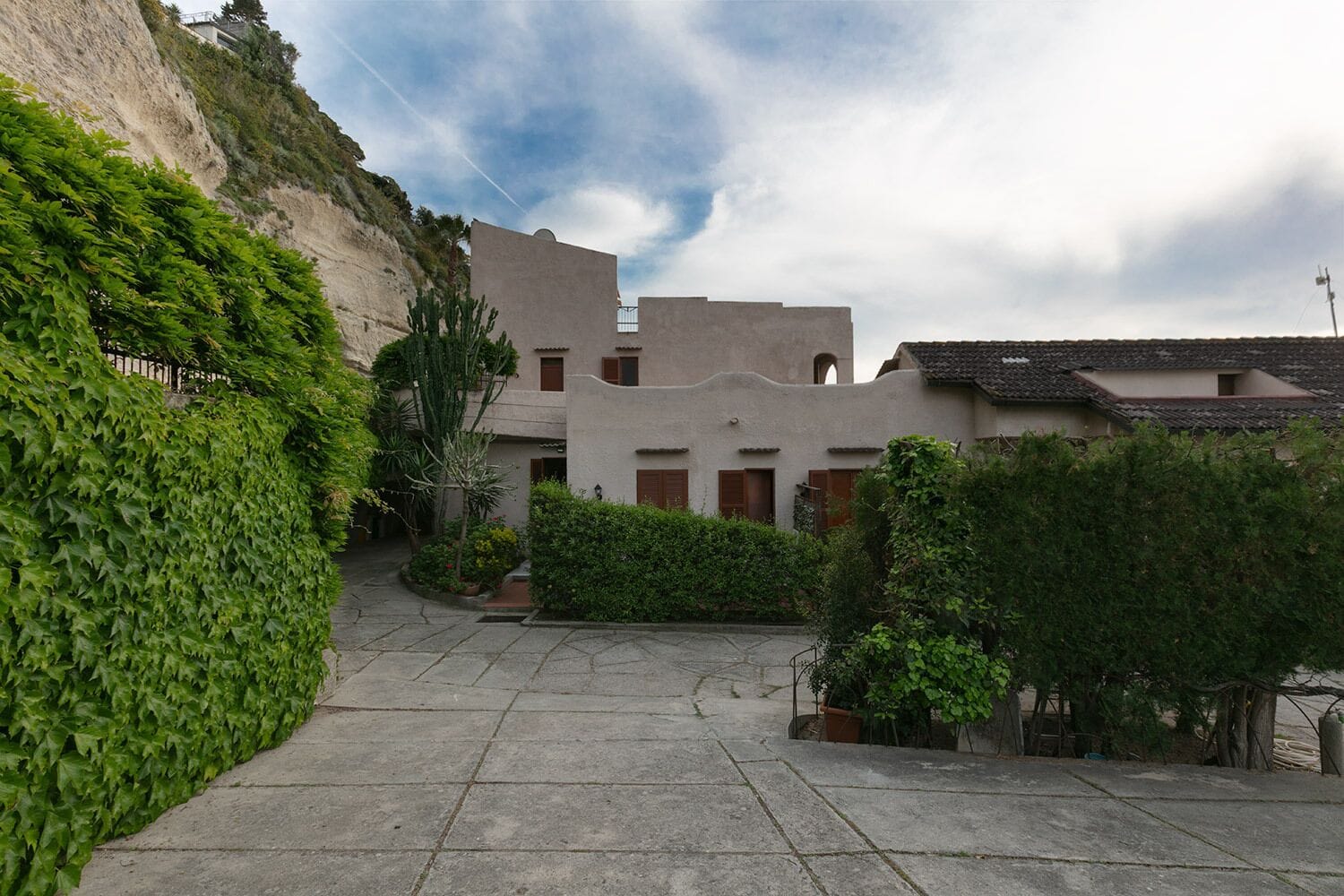 A courtyard with a stone pathway leading to a building with a flat roof and a small balcony.