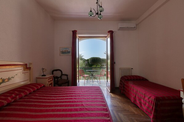 A bedroom with two beds, a desk, a chair, and a balcony with a view.
