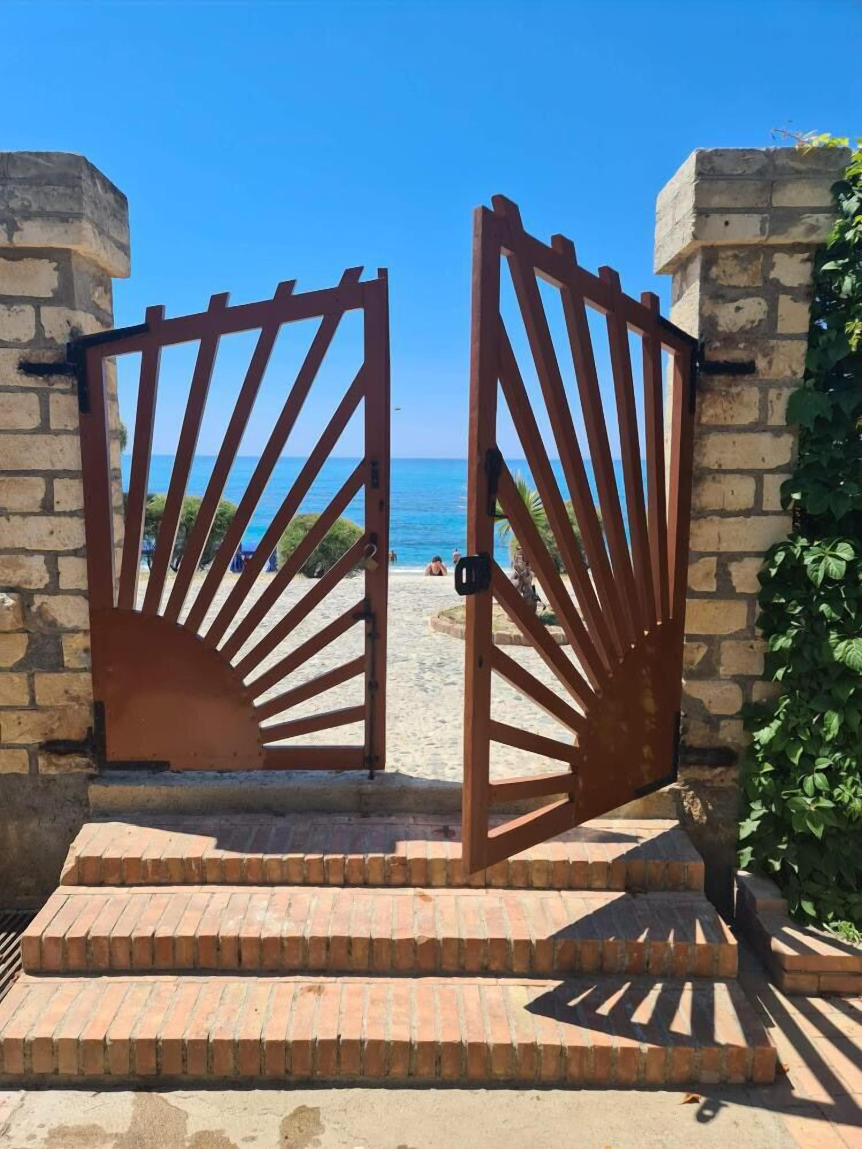 A set of wooden gates leading to a beach area with a clear view of the sea.