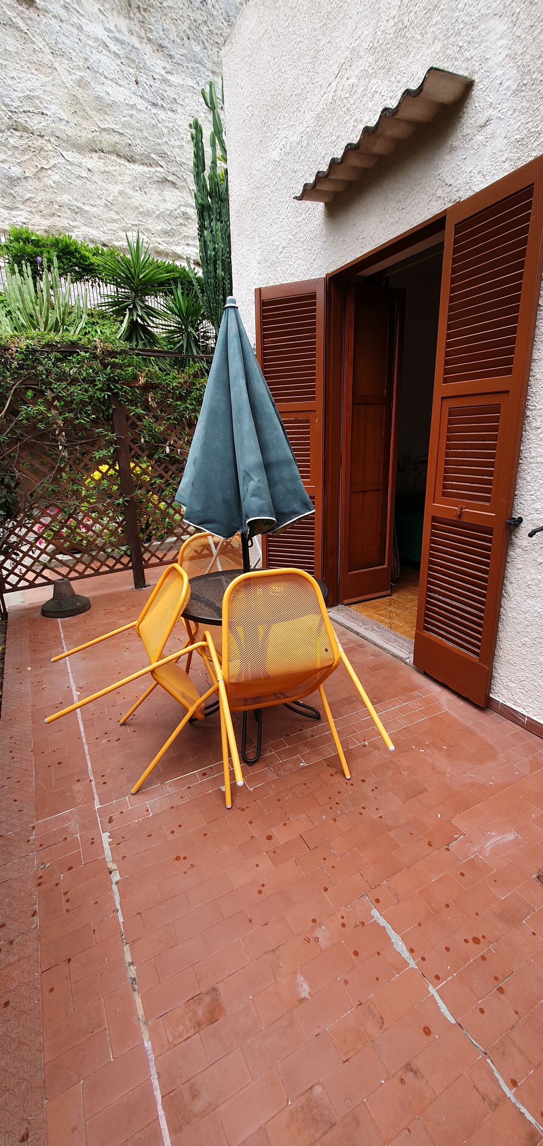 A patio with a table and chairs, a blue umbrella, and a wooden door.