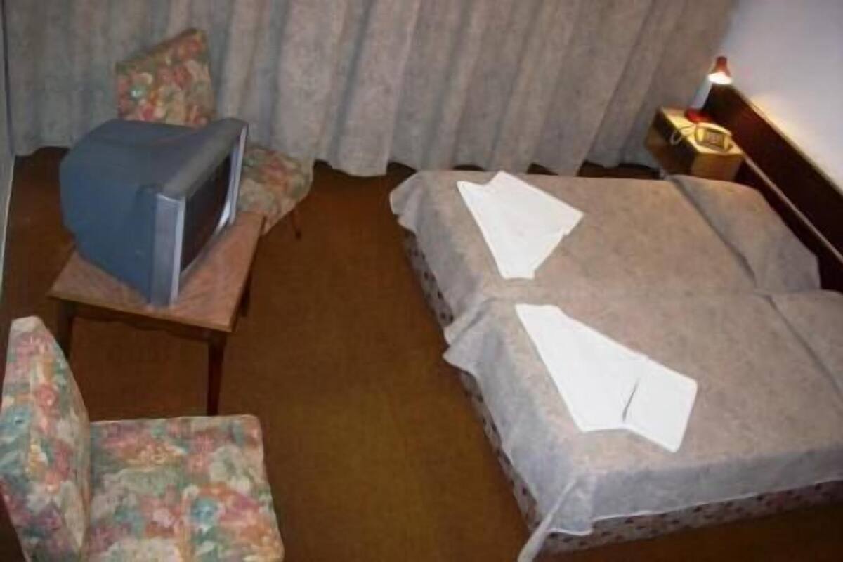 Hotellihuone, jossa on sänky, tuoli, televisio ja yöpöytä, jossa on lamppu.