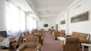Ein geräumiger Raum mit mehreren Sofas und Sesseln, die in einer Reihe angeordnet sind, einem an der Wand montierten Flachbildfernseher und einer Kandelaberleuchte an der Decke.