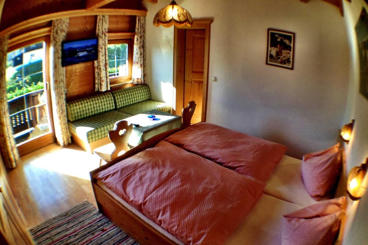 A cozy room with a bed, a small table, and a window overlooking greenery.