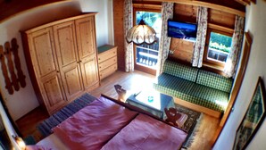 A room with a bed, a wooden wardrobe, a television, and a window with curtains.