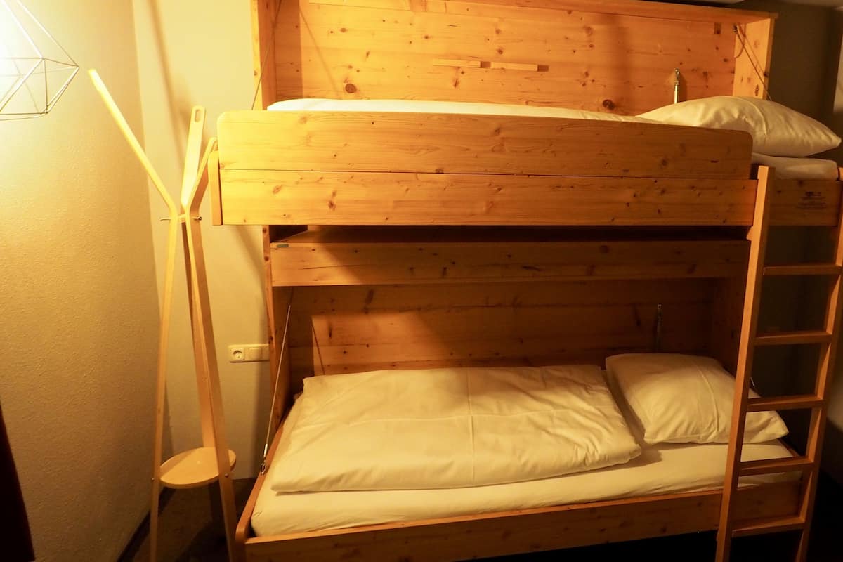 A bunk bed with a ladder, a bedside table, and a wall socket.