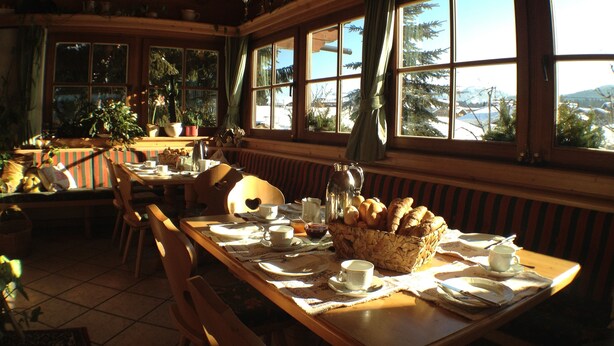 A cozy dining area with wooden furniture, large windows, and a view of trees and mountains.