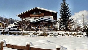 A large wooden building with a sloped roof, surrounded by snow-covered ground and trees.