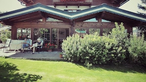 A wooden chalet with a balcony, large windows, and a covered patio area.