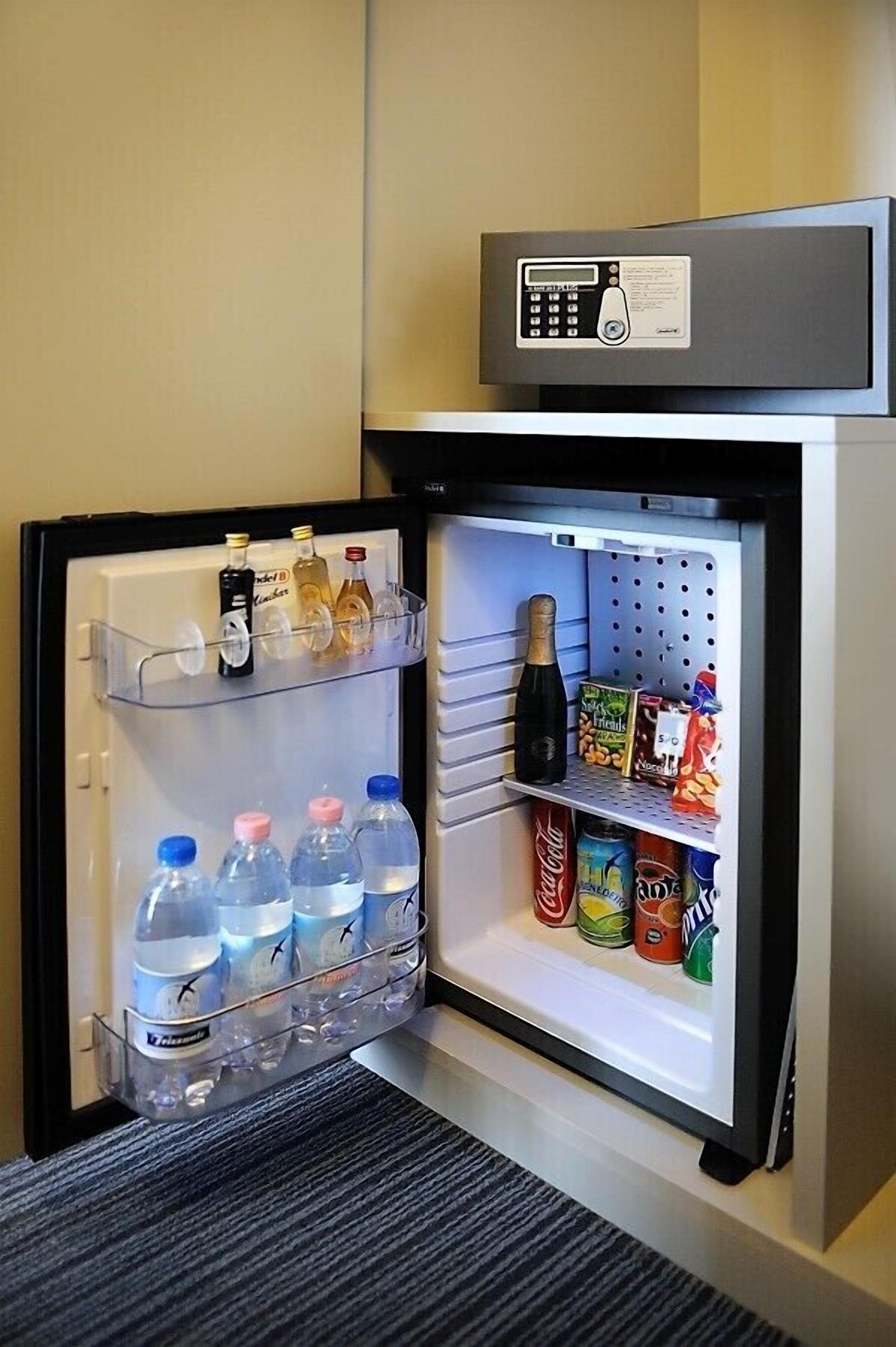 A mini-fridge with a digital lock, containing bottled water, soda, and snacks.