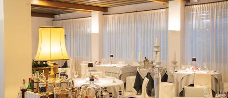 Une salle à manger avec des tables dressées pour le service, une variété de bouteilles d’alcool et une grande lampe.