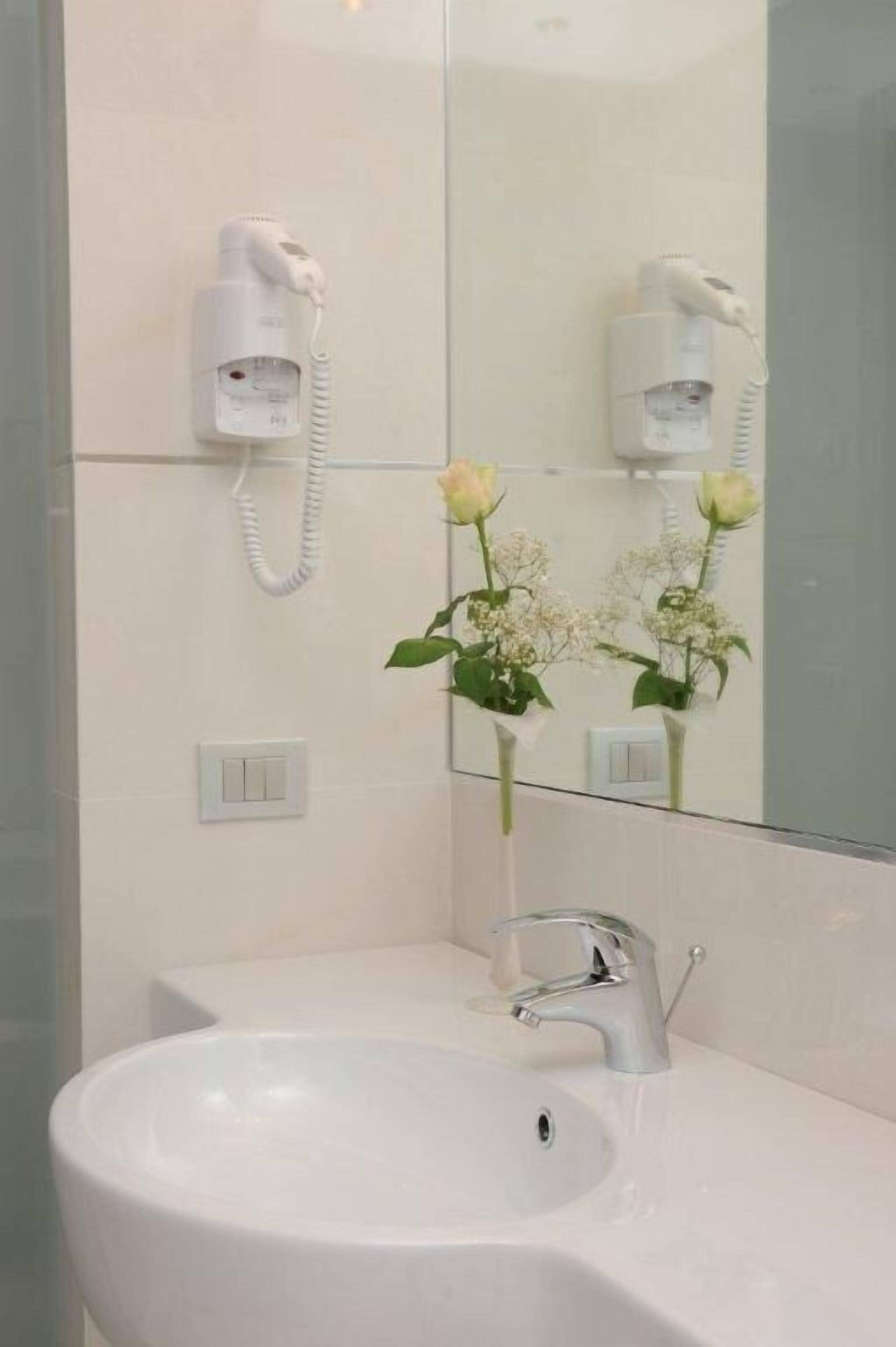 Une salle de bain avec un lavabo blanc, un miroir et un sèche-cheveux fixé au mur.
