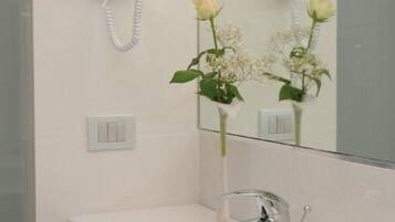 Une salle de bain avec un lavabo blanc, un miroir et un sèche-cheveux fixé au mur.