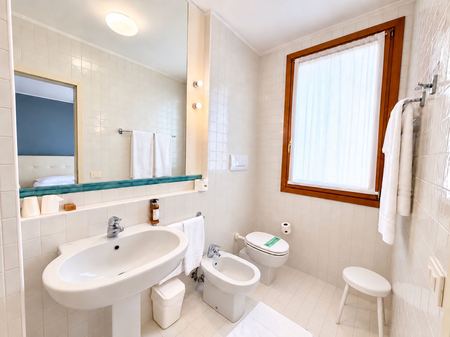 A modern bathroom with a large mirror, a sink, a bidet, a toilet, and a window.