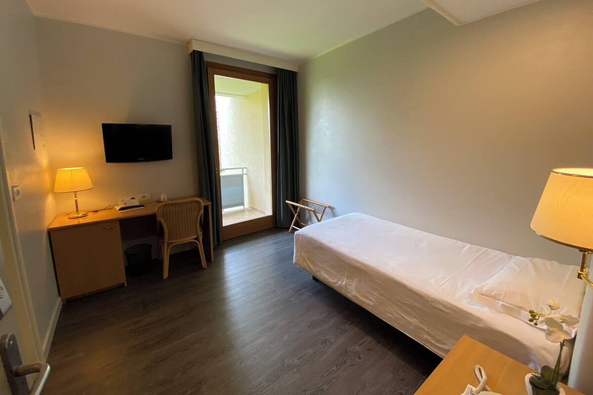 A hotel room with a bed, desk, chair, TV, and a window with curtains.