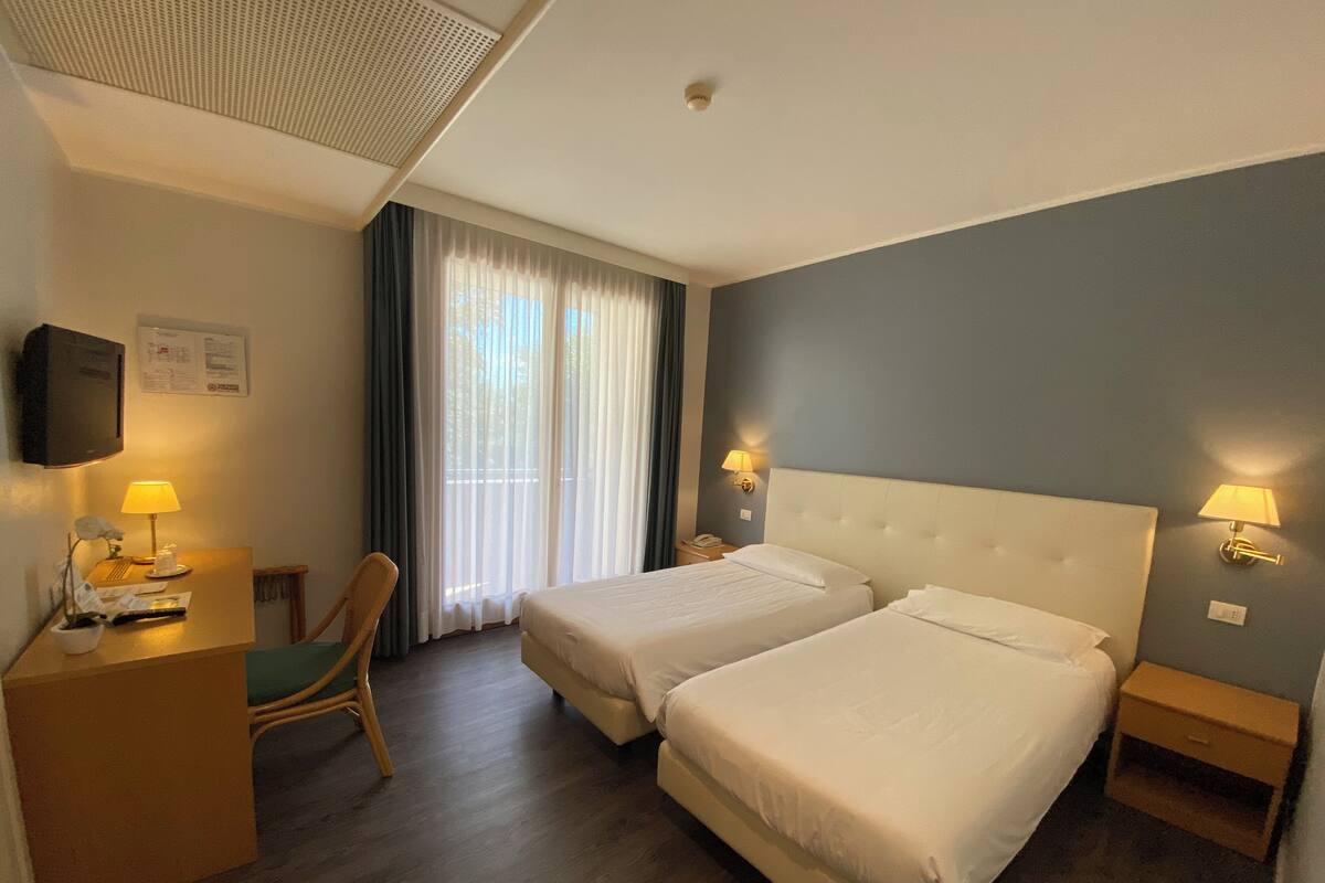 A hotel room with two beds, a desk with a chair, a TV, and a window with curtains.