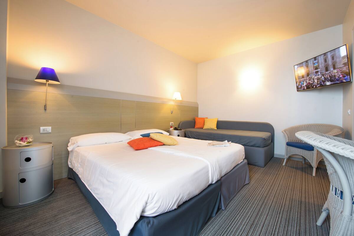 A hotel room with a large bed, a sofa, a small table, and a TV mounted on the wall.