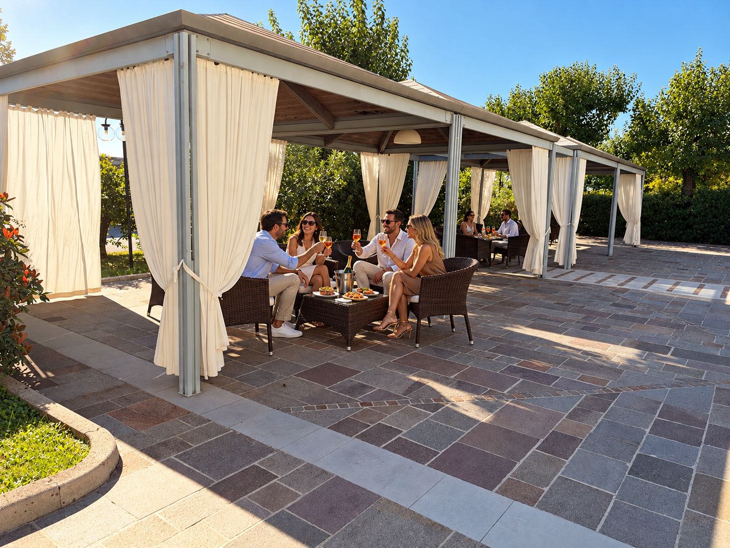 Eine Terrasse im Freien mit überdachter Sitzgelegenheit, Steinboden und einer Gruppe von Personen, die speisen.