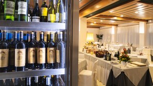 A wine refrigerator stocked with various bottles, a dining area with tables set for guests, and a ceiling with wooden beams.