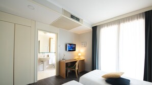 A hotel room with a bed, a desk with a chair, a television, and a bathroom visible through an open door.