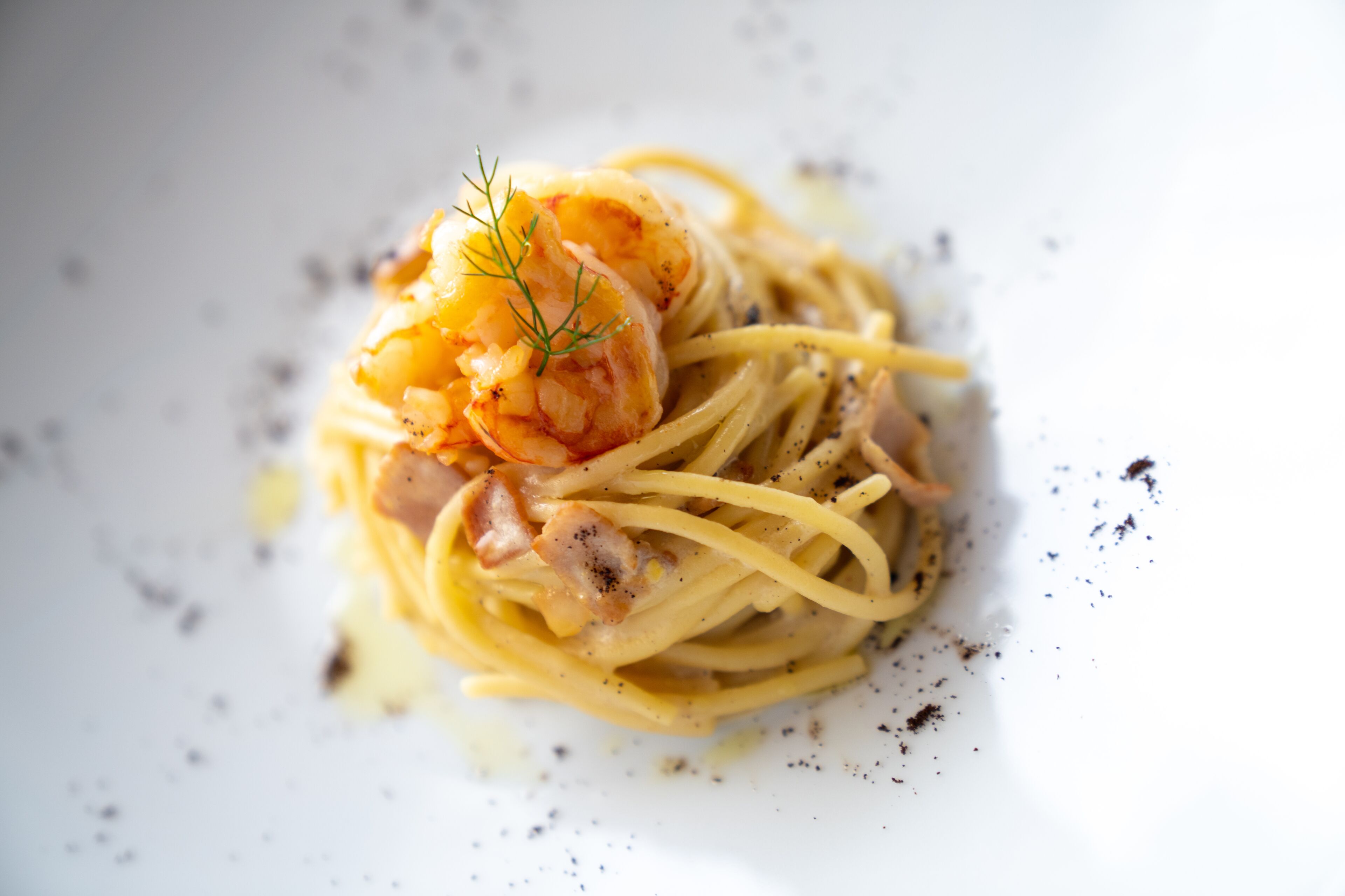 Un piatto di spaghetti con gamberi e pancetta, guarnito con un rametto di aneto.