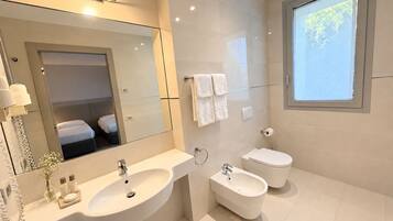 A modern bathroom with a large mirror, a double sink, a bidet, and a toilet.
