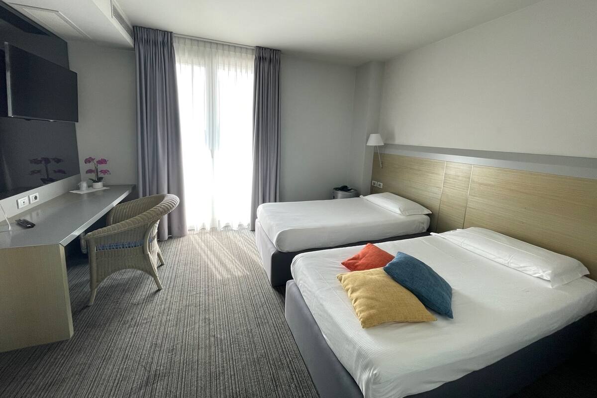 A hotel room with two beds, a desk, a chair, a TV, and a window with curtains.