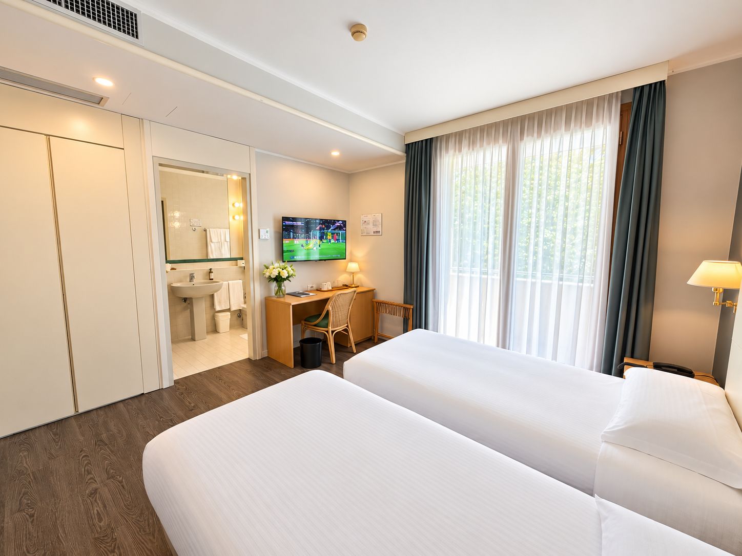 Ein Hotelzimmer mit zwei Betten, einem Schreibtisch, einem Fernseher und einem Badezimmer.