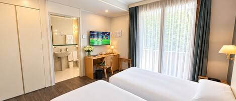 A hotel room with two beds, a desk, a TV, and a bathroom.