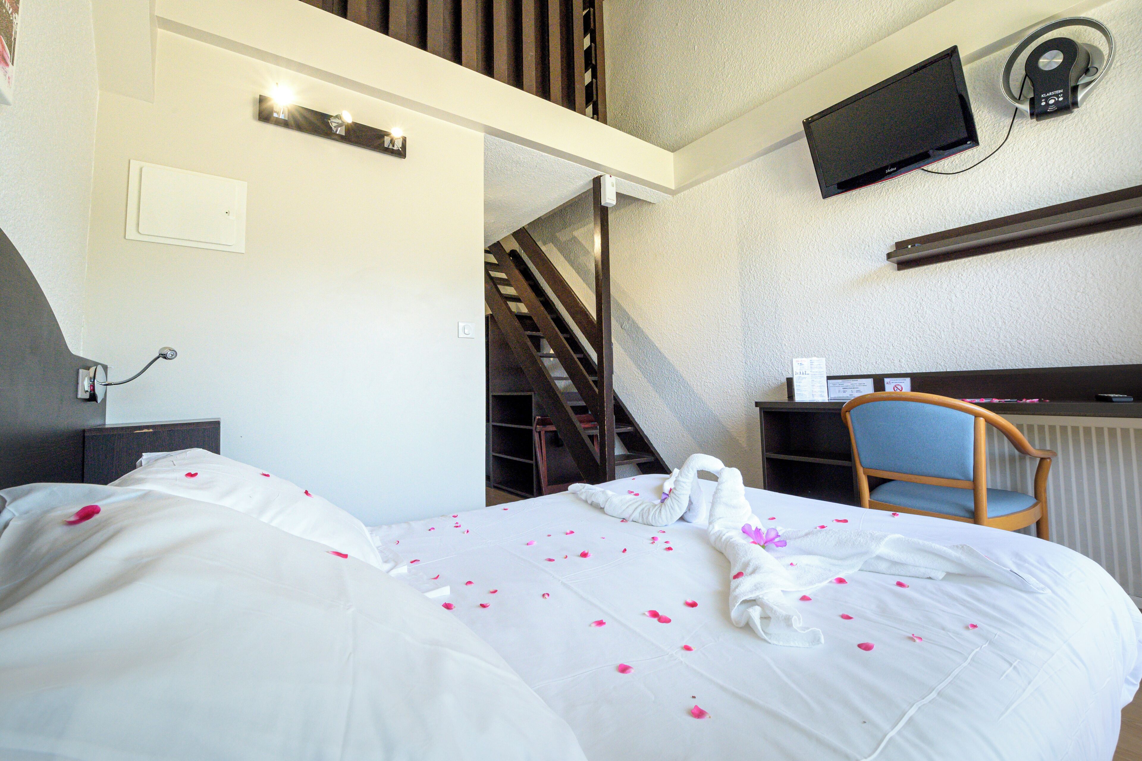 A hotel room with a bed, a desk, a chair, a television, and a staircase.