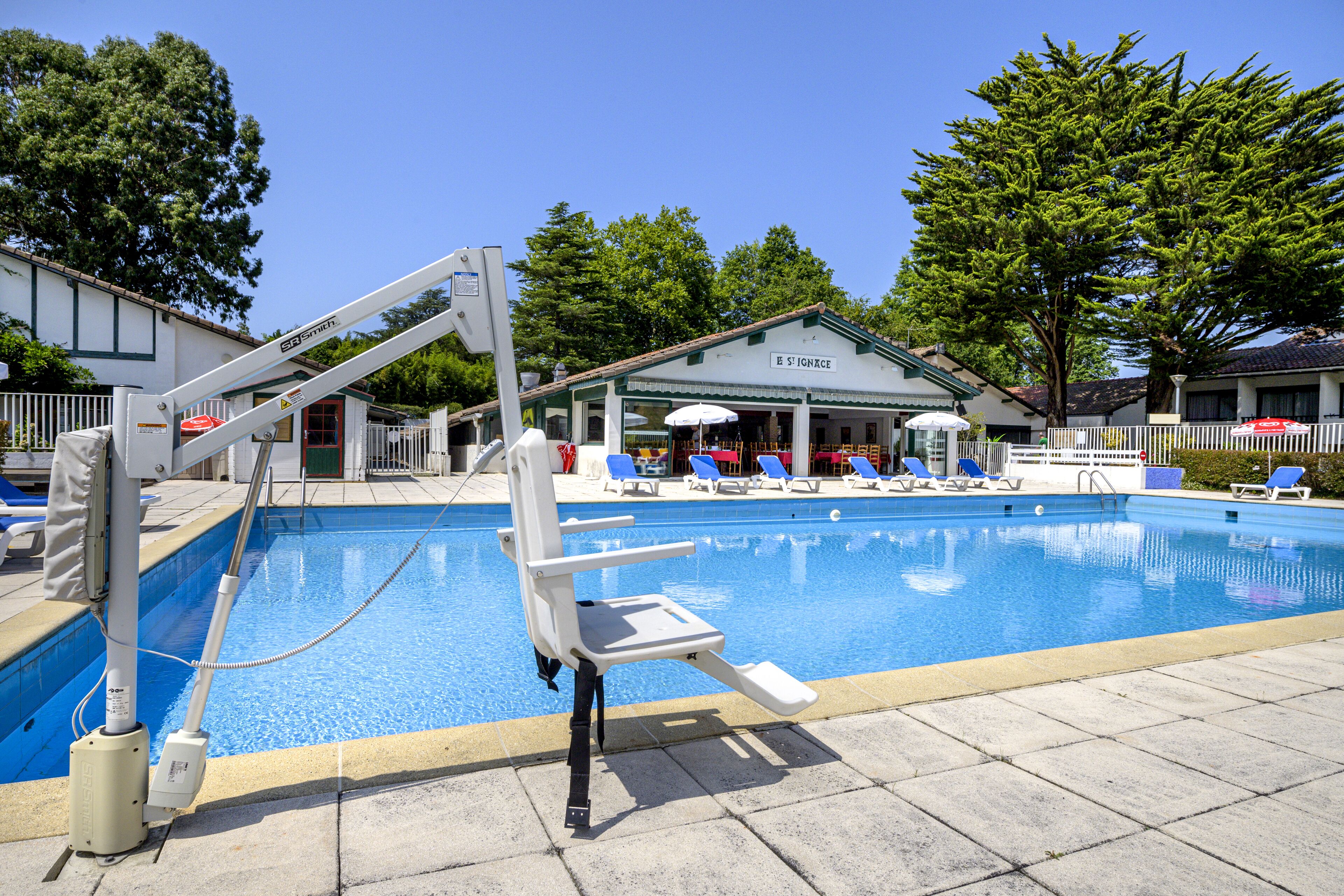 A swimming pool with a lifeguard chair, lounge chairs, and a building with a sign in the background.